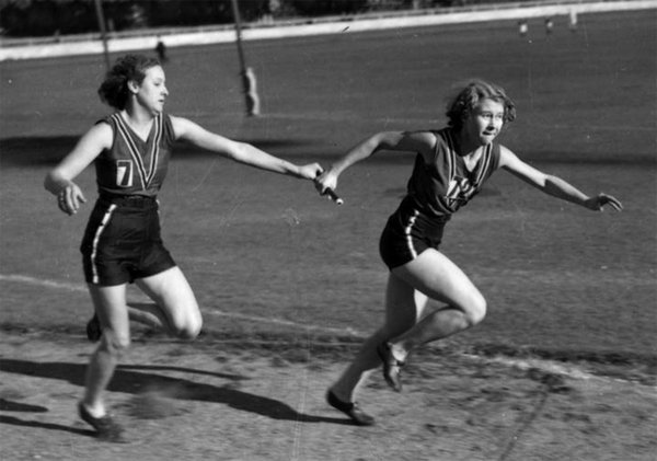Schwarzweiß-Foto von zwei Staffelläuferinnen, die die Staffel übergeben